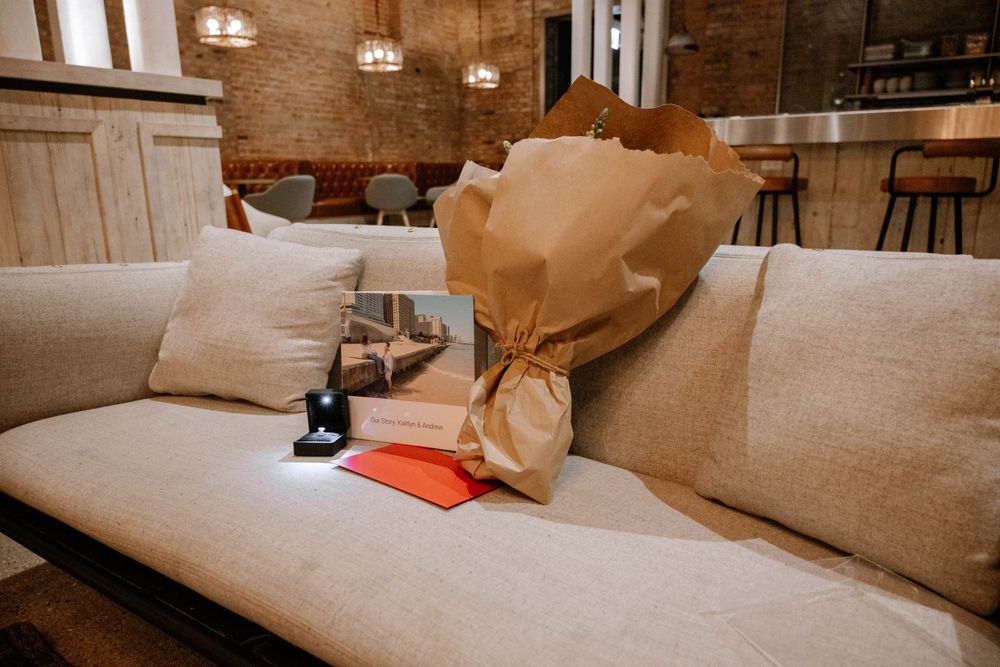 A beige couch with throw pillows and a takeout paper bag sitting on the cushions in a rustic interior setting.