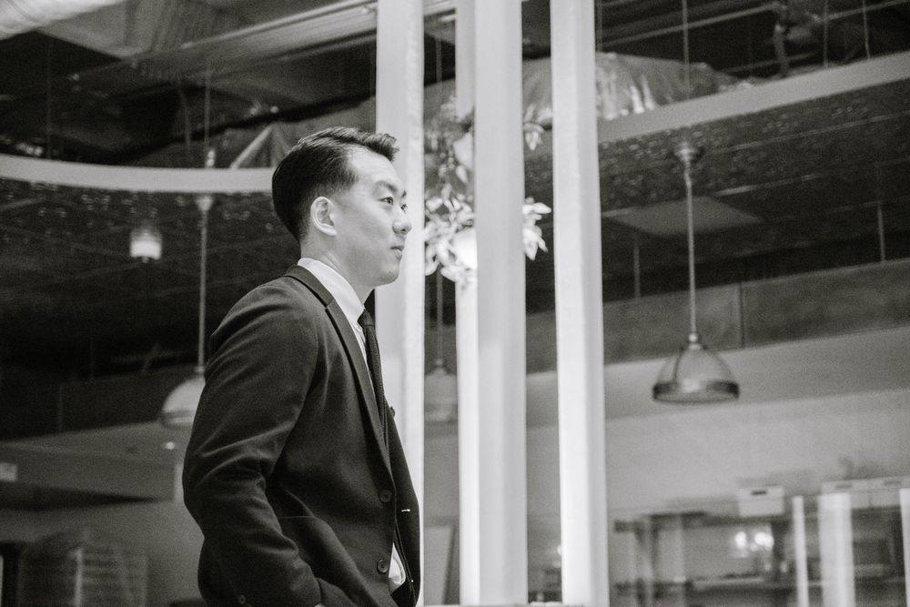 A person in a business suit stands thoughtfully next to white pillars in an industrial interior space.