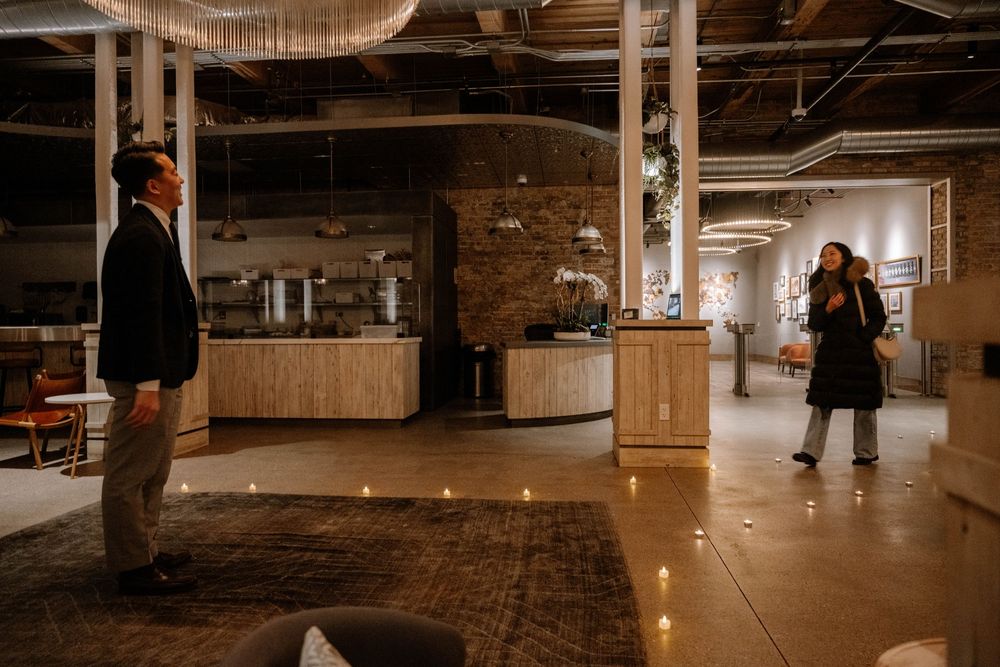 People standing in an industrial-style venue with exposed brick walls, wooden fixtures and hanging light fixtures.