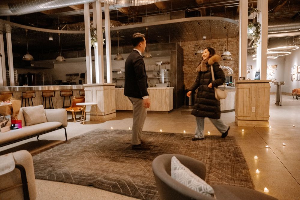 Two people converse in a modern industrial-style space with wooden furniture and warm lighting.