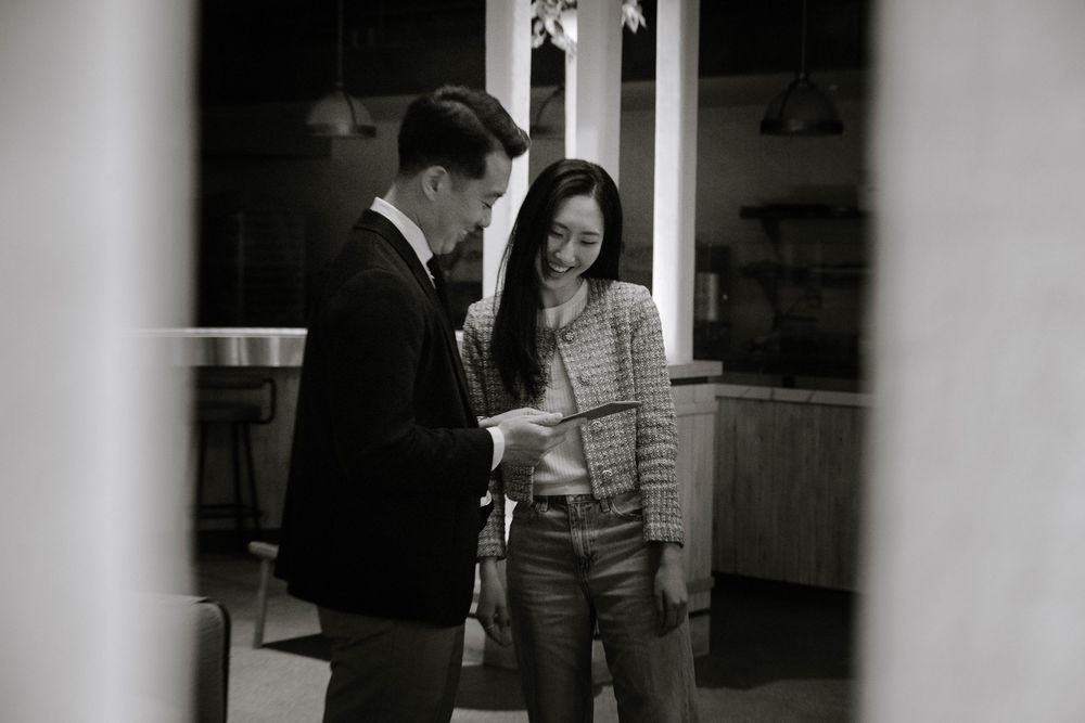 Two people in professional attire having a conversation while looking at documents in a black and white photograph.
