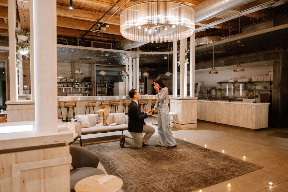 A marriage proposal inside an elegant industrial venue with chandeliers and romantic candle lighting.