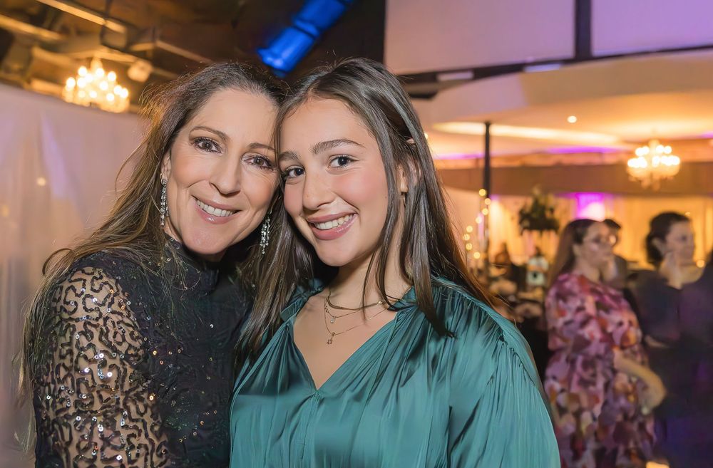 Two people in evening attire pose for a photo at an indoor event with decorative lighting in the background.