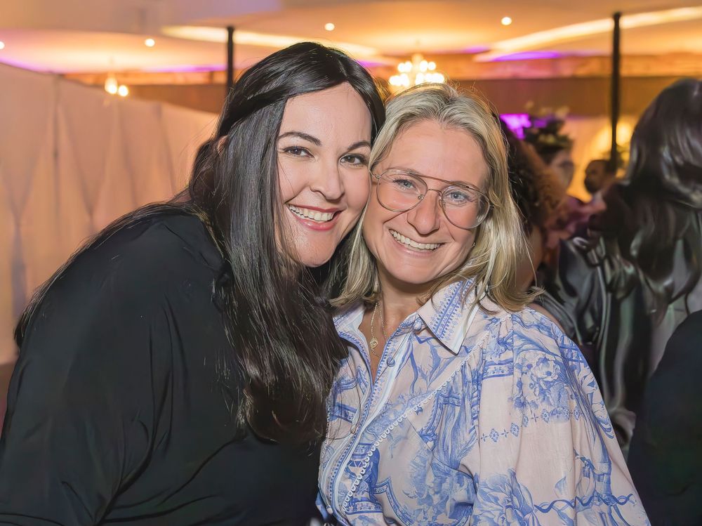 Two people smiling together at an evening event with warm lighting in the background.