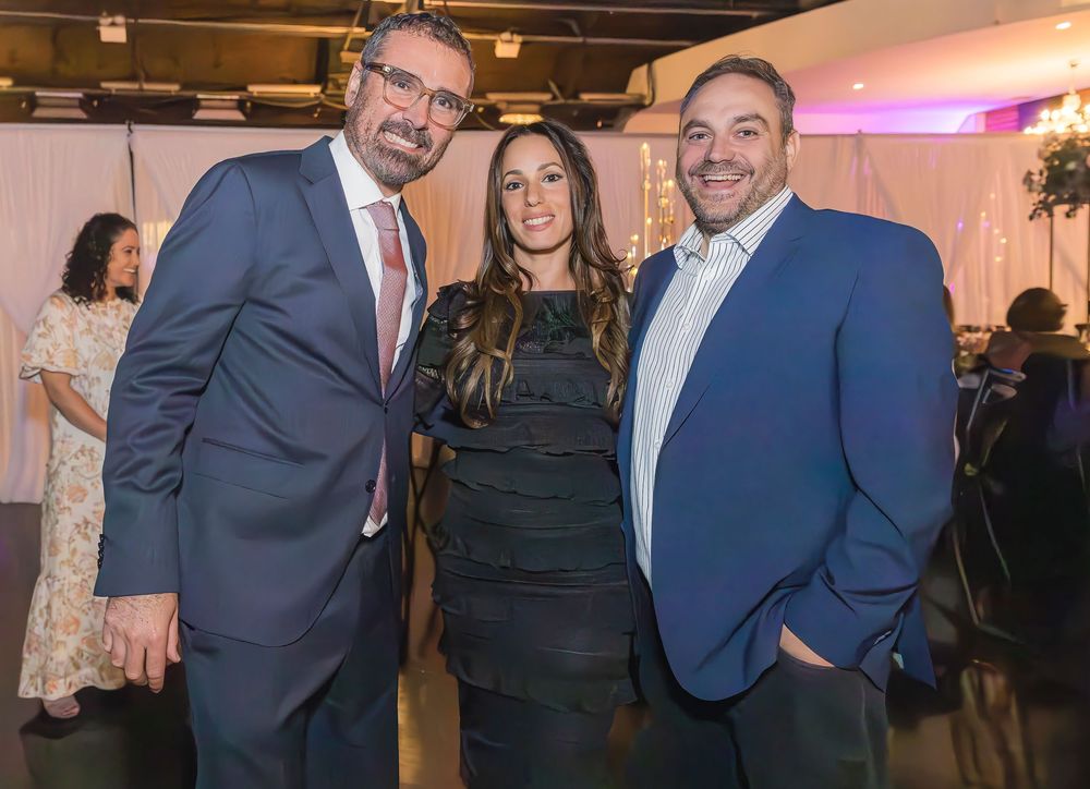 Three well-dressed professionals posing together at an indoor networking event with dim lighting.