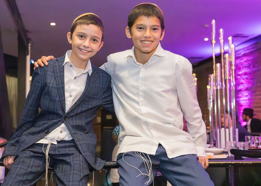 Two young people in formal attire sit casually at an event with purple lighting and decorative candles in background.