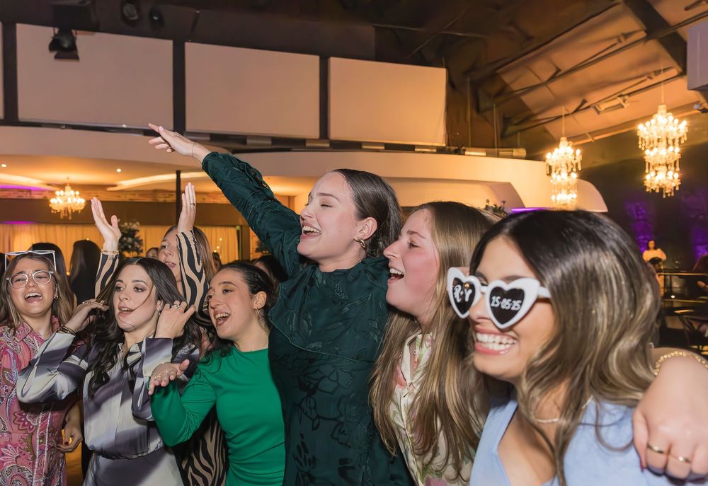 People having fun at a party event singing karaoke together while wearing party sunglasses under chandeliers.