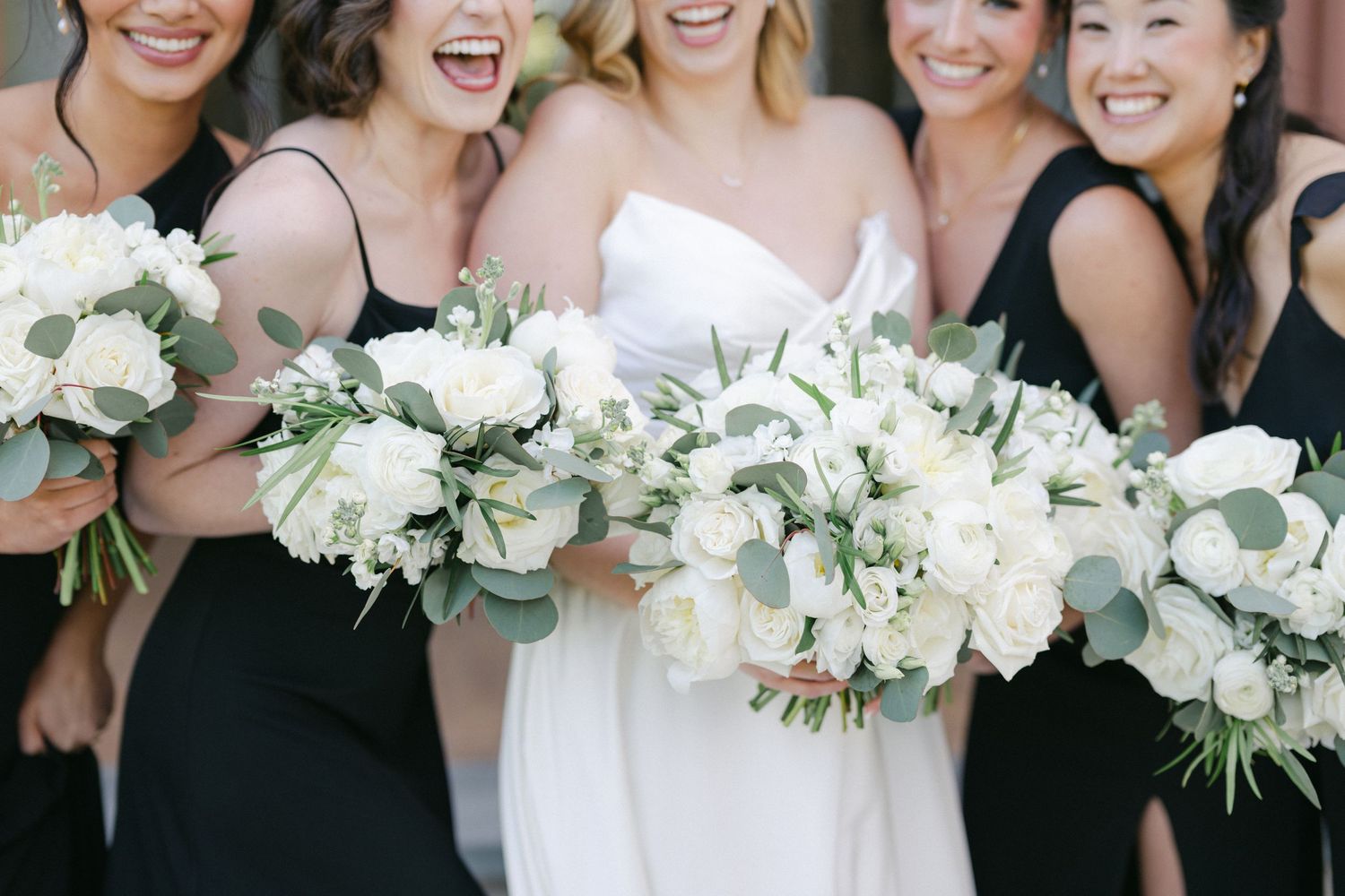 Wedding party holds elegant white floral bouquets while wearing black bridesmaid dresses and white bridal gown.