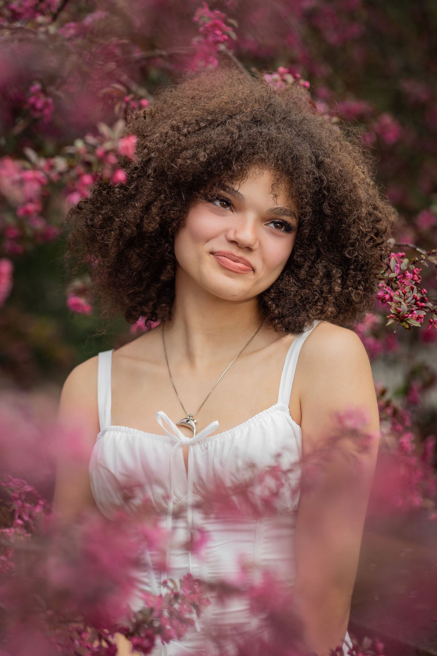 Portrait with natural curly hair and black sweater amid blooming pink cherry blossoms in soft focus.