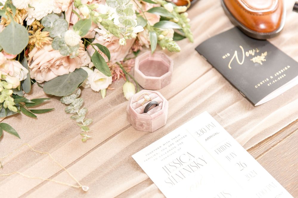 Wedding details featuring floral arrangements, pink drinks, and stationery on a wooden surface.