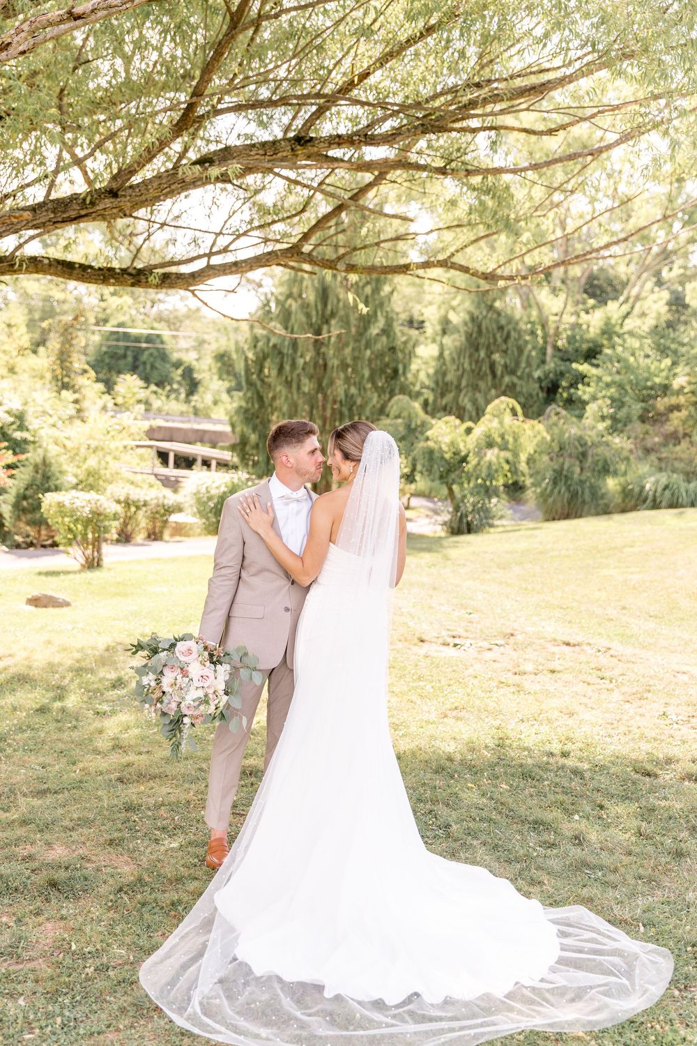 Newlywed couple sharing an intimate moment on their wedding day under a tree with a flowing white veil.