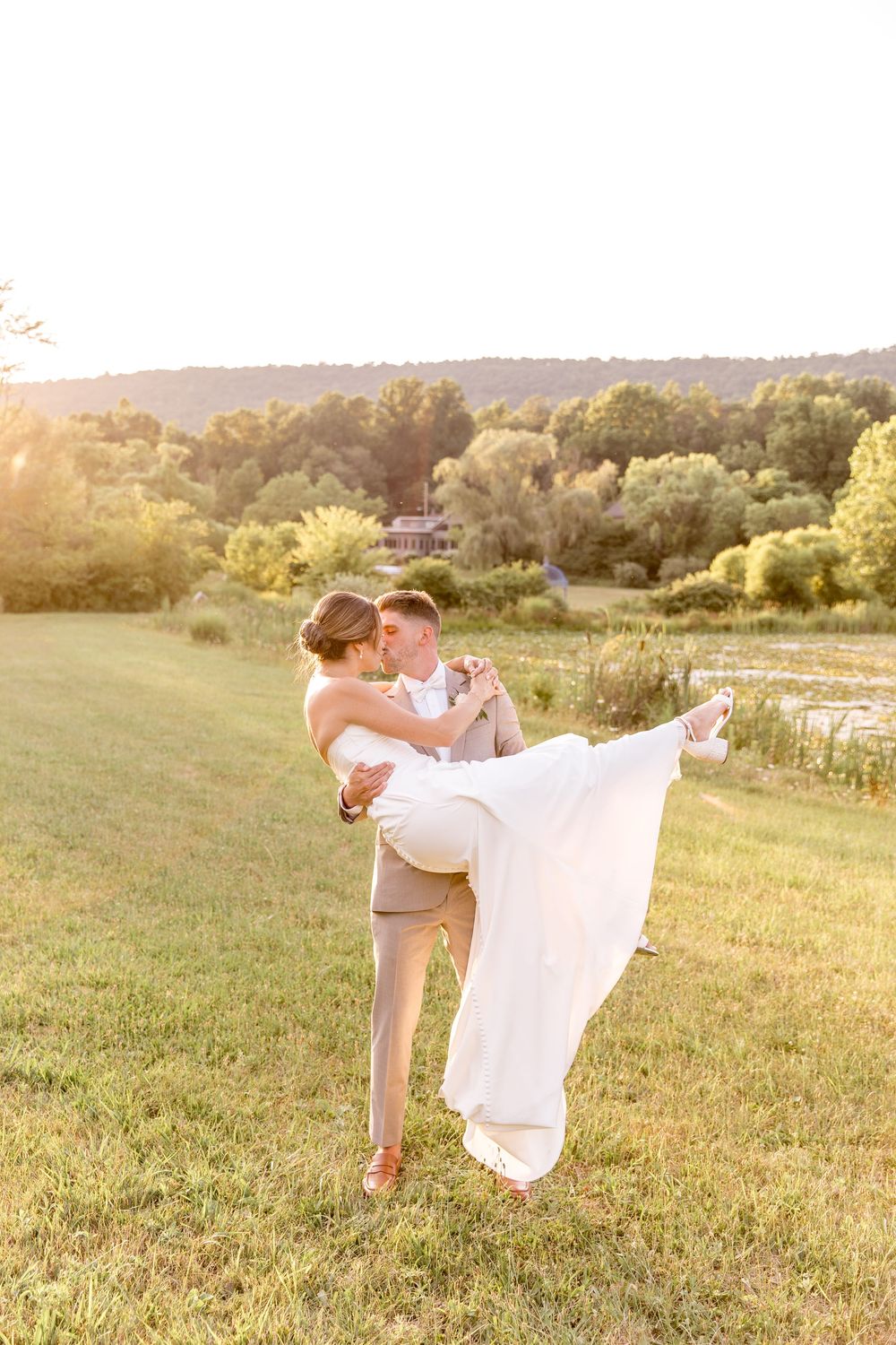 A romantic wedding moment captured in a sunlit meadow as a couple embraces in golden hour light.