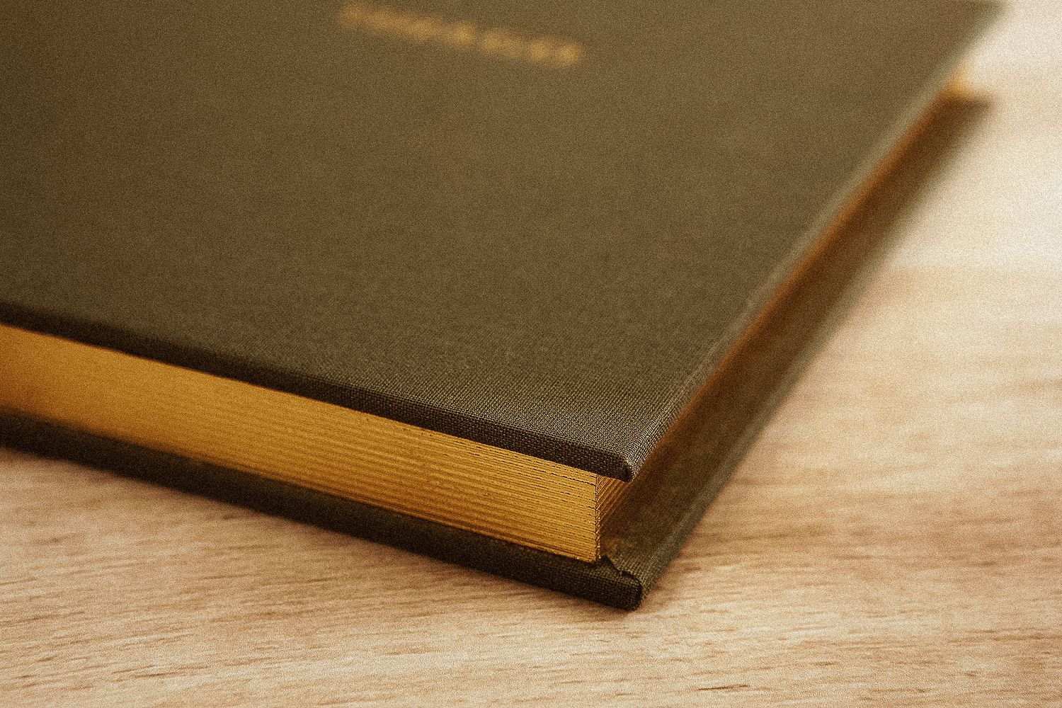 Close-up shot of a hardbound book with a brown cover and golden textured pages resting on a wooden surface.
