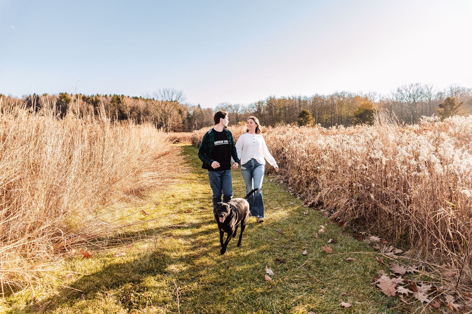 Two people enjoy a bike ride together on a grass path surrounded by tall autumn grasses on a sunny day.