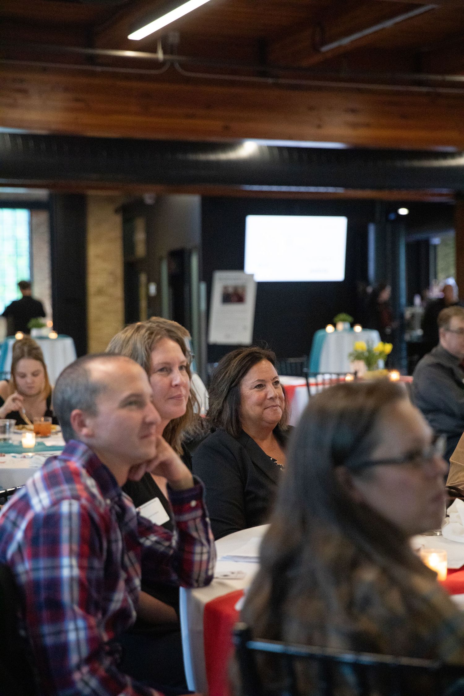 Business conference attendees listening intently during a presentation in a rustic venue with wooden beams.