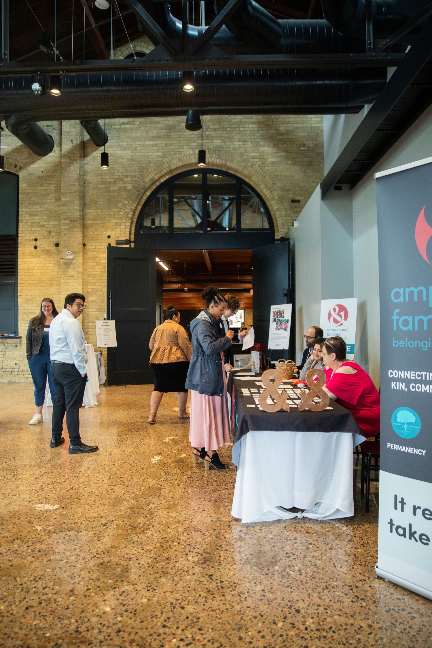 People gather around registration tables at a business event with brick walls and arched doorways.