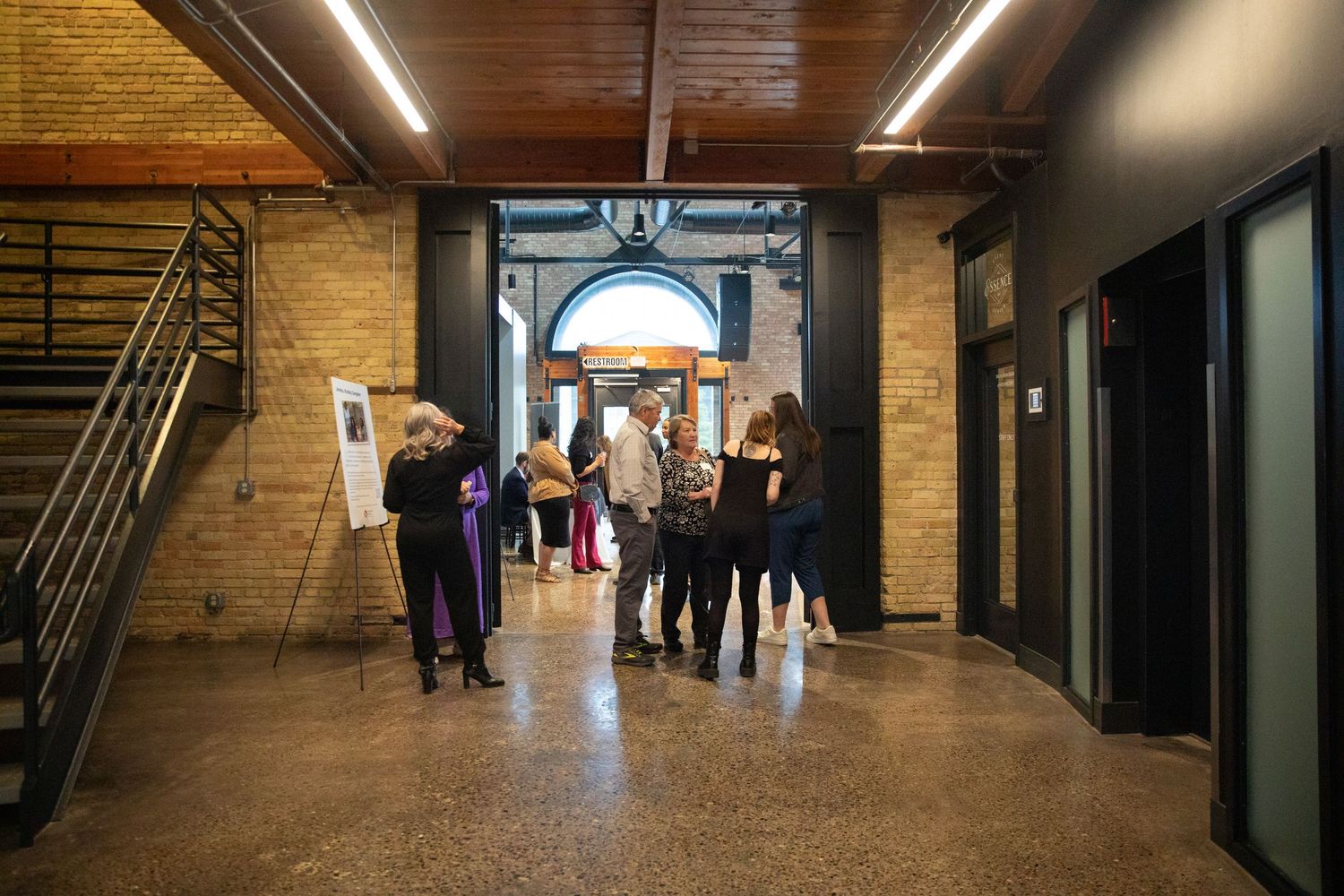 People gather in a modern industrial hallway with brick walls and an arched doorway.