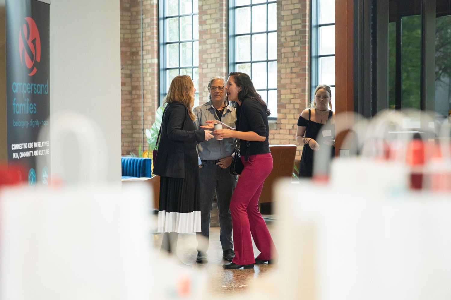 People having a conversation in a modern event space with brick walls and tall windows.