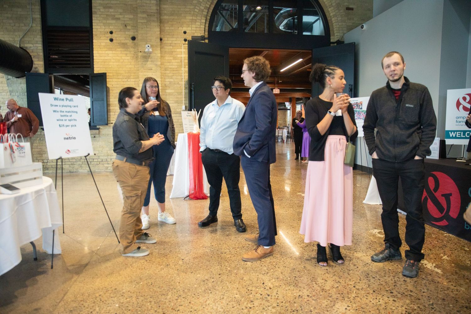 A group of people mingle and socialize at a casual indoor event near an entrance doorway.