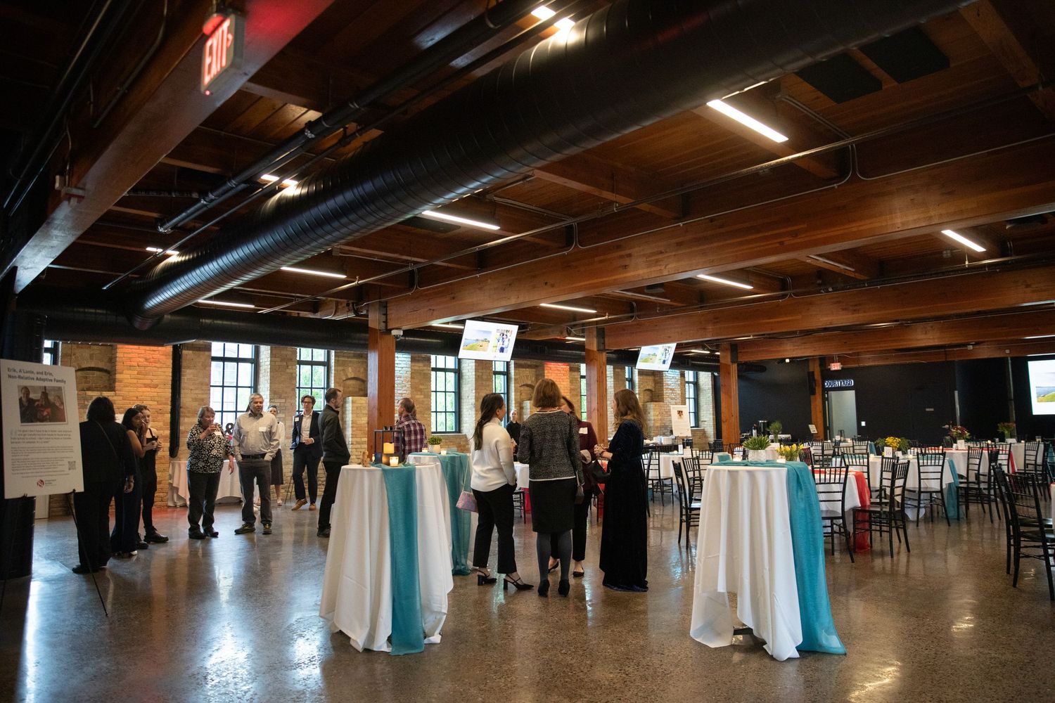 Conference venue with exposed wooden beams and high tables where attendees network during an event.