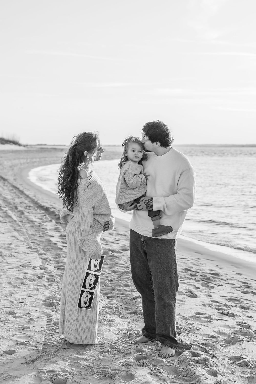 Family shares pregnancy announcement moment on a beach with ultrasound photos.