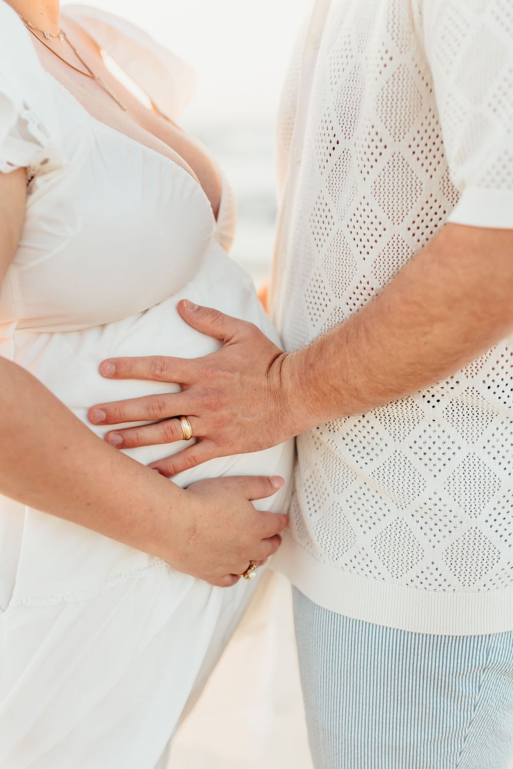 Close-up of gentle embracing hands against white clothing. Sunset Wrightsville beach wilmington nc. Maternity sunrise beach photography.