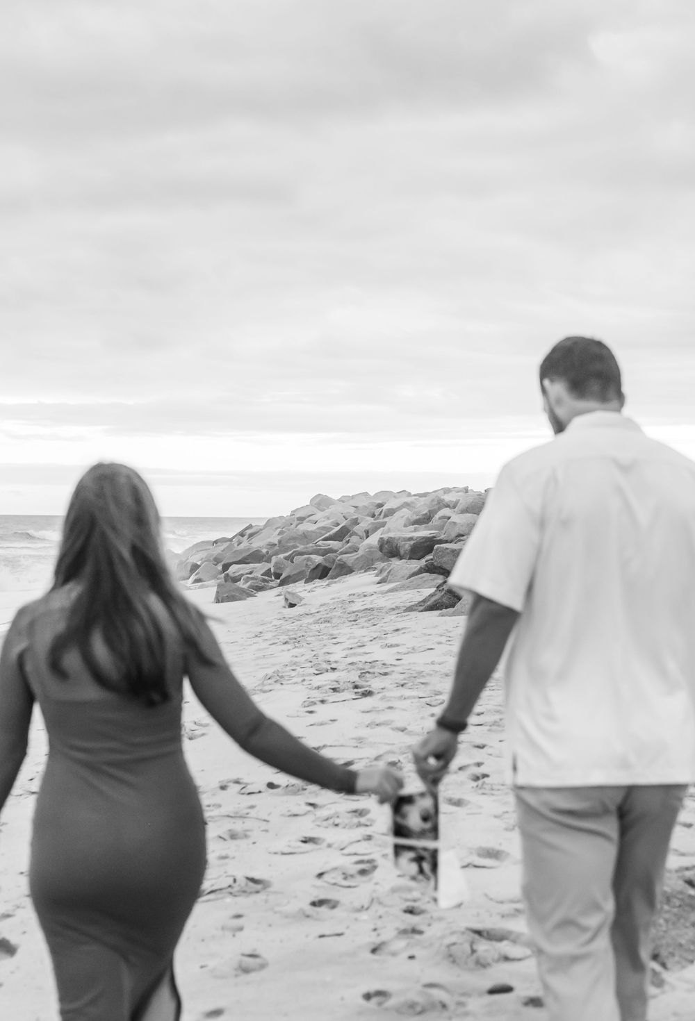 Couple walking hand in hand along a rocky beach shoreline.