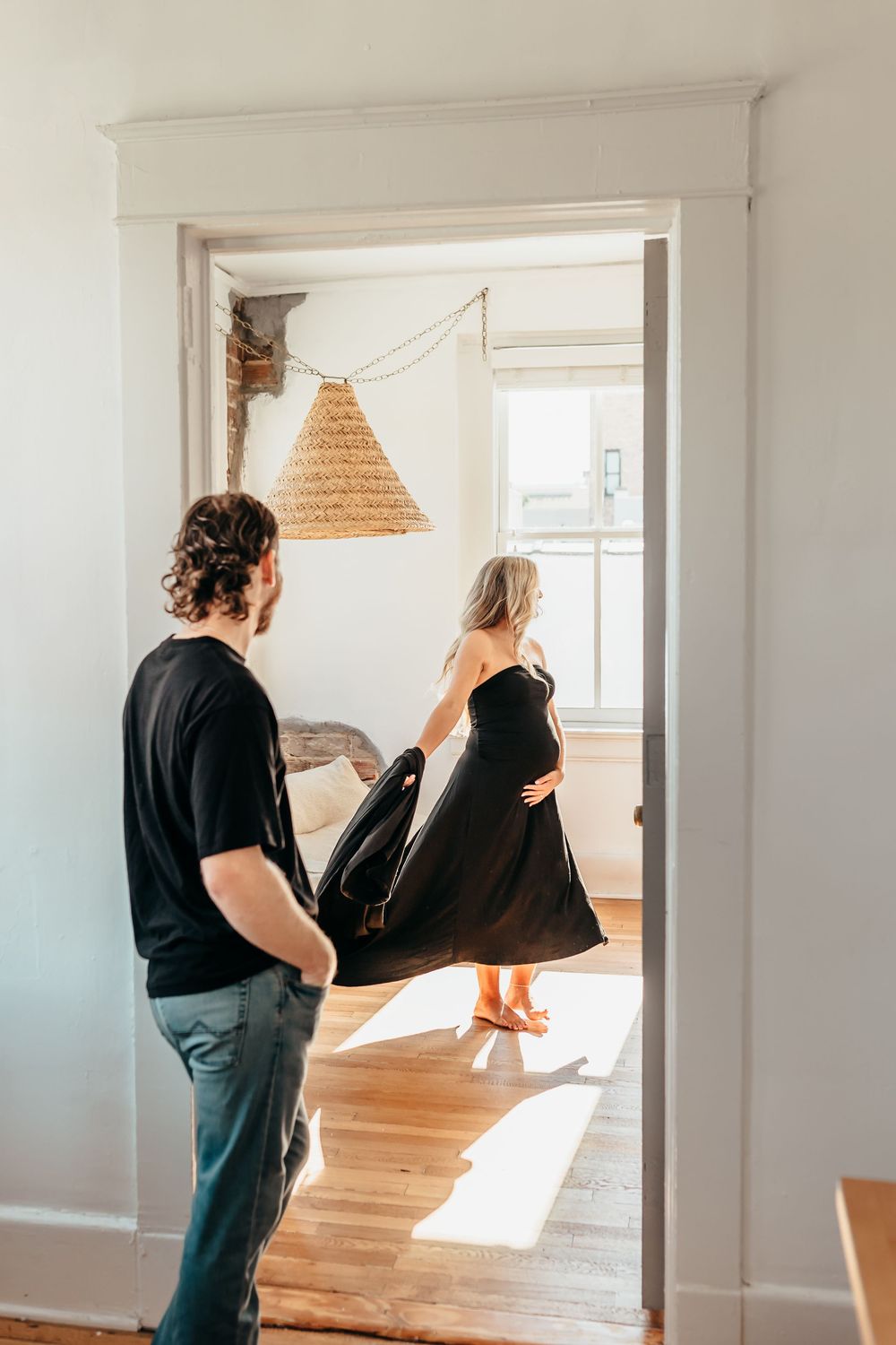Two people dance together in a sunlit room with hardwood floors and a woven pendant lamp hanging from above.