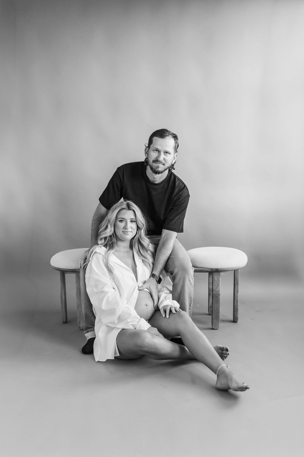 A couple in monochromatic tones poses intimately on a minimalist studio floor in a series of artistic shots.