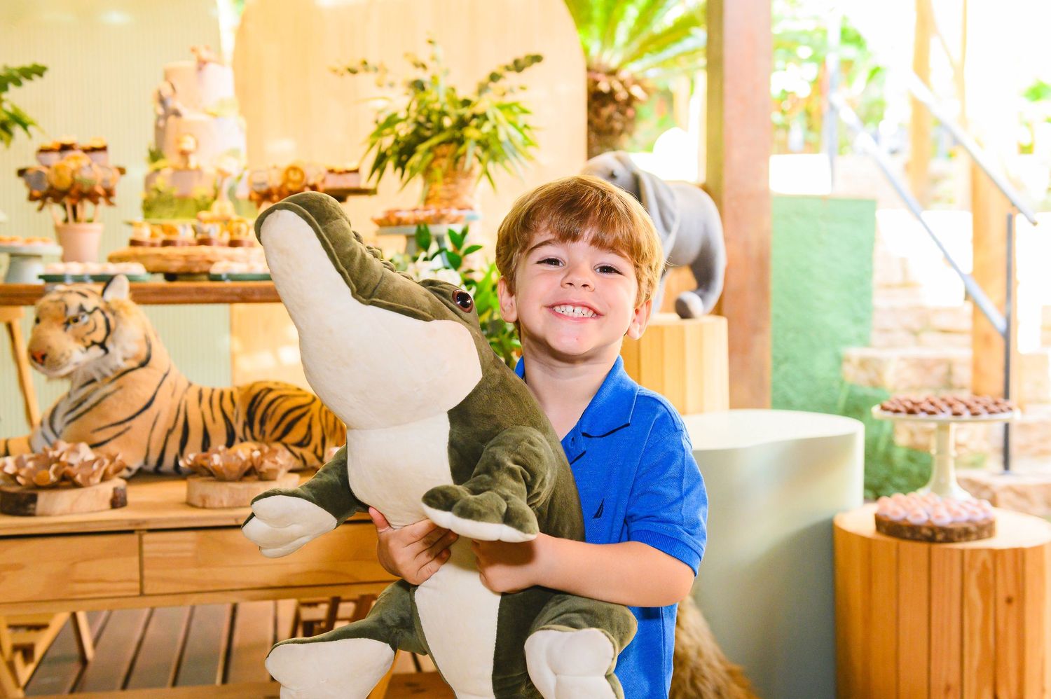 Child sits at party table decorated with stuffed animals and ornate decor for a special celebration.