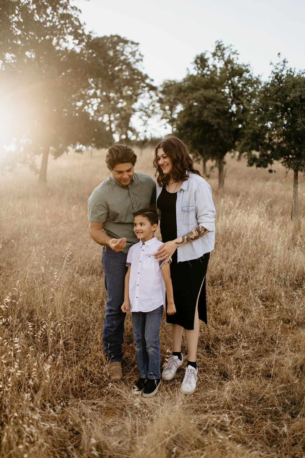 A family stands together in a golden field at sunset, creating a warm and intimate outdoor portrait.