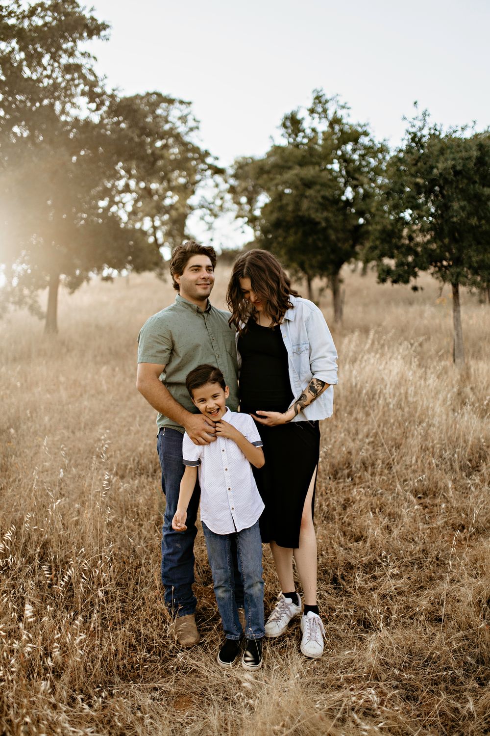 A family stands together in a sun-drenched field with golden grass and trees in the background during sunset in Rescue.