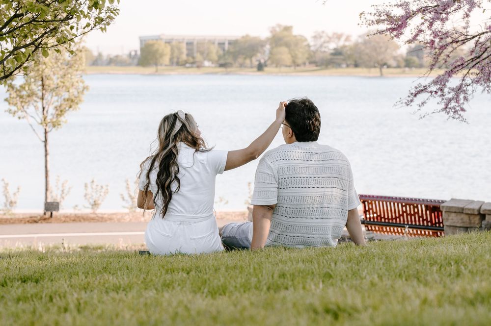 A couple sits together on grass by a lake with a picnic basket during a peaceful afternoon.