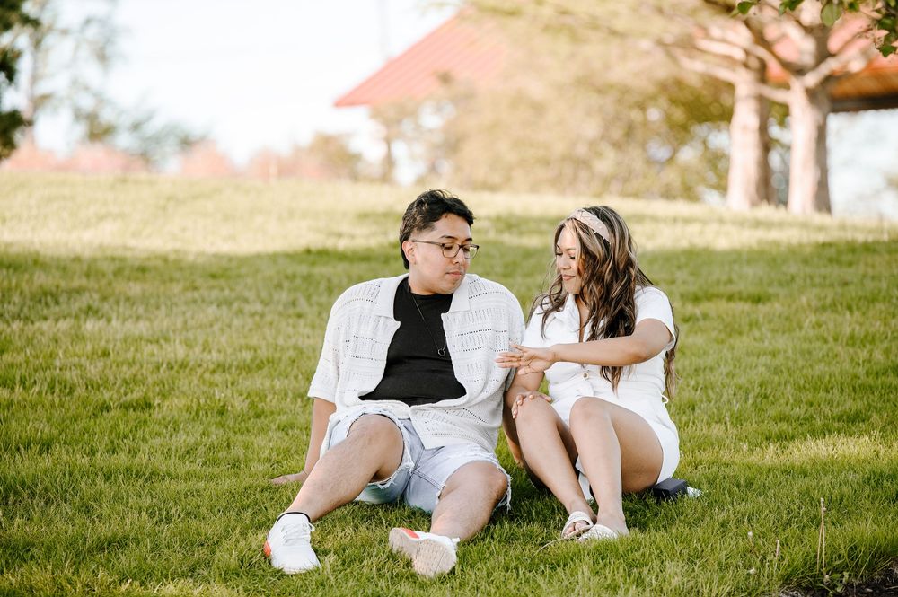 A couple sits close together on a grassy slope having an intimate conversation outdoors.