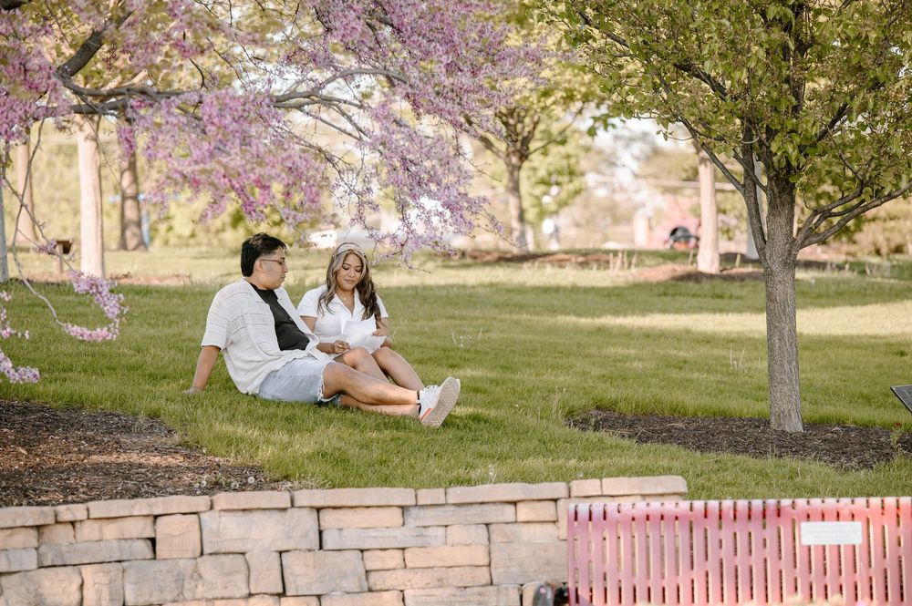 A couple enjoys a peaceful moment sitting on a stone retaining wall under blooming spring trees.