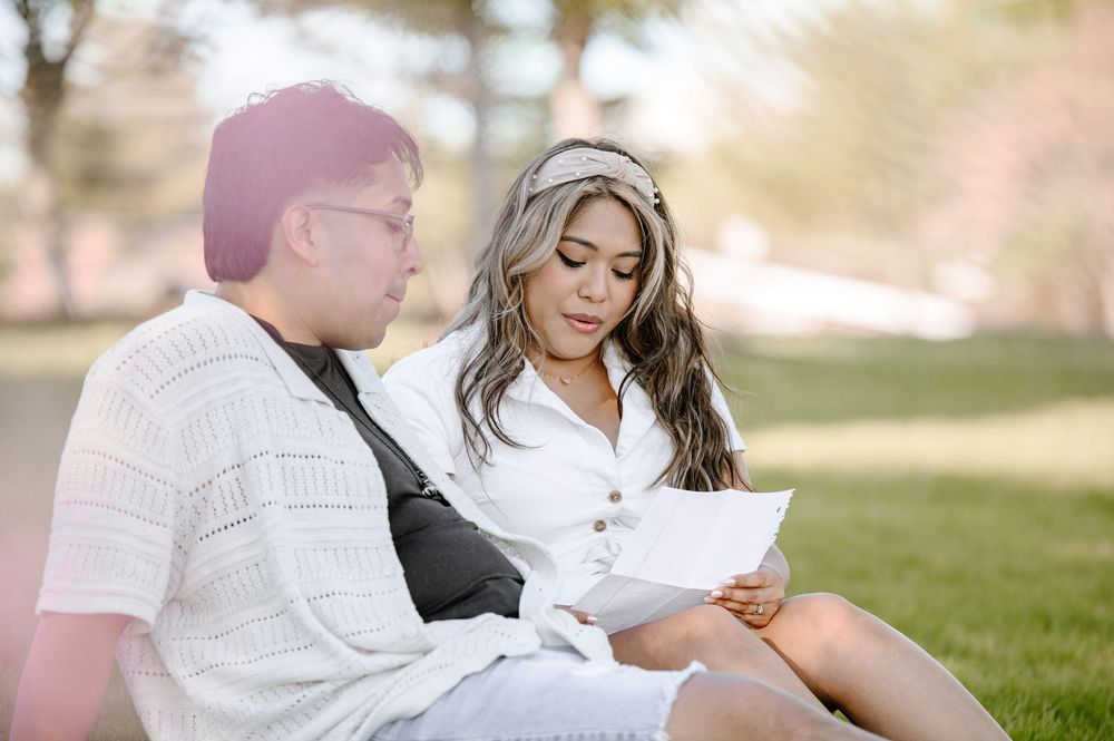 Two people sitting together on grass reading documents on a sunny day in the park.