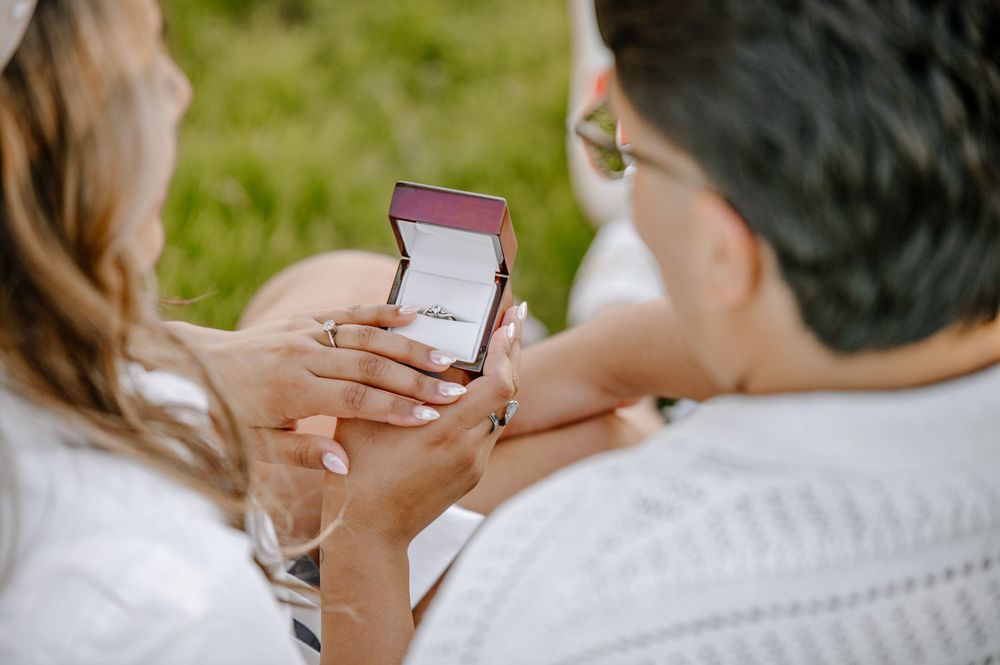Close up view of hands holding a small ring box during an outdoor engagement proposal.
