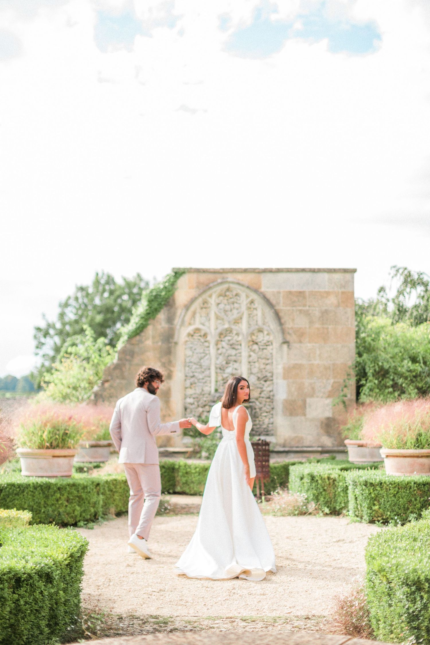A couple stands together at a garden path with ornate stone architecture for their Italian wedding by Hayley Elizabeth Photography