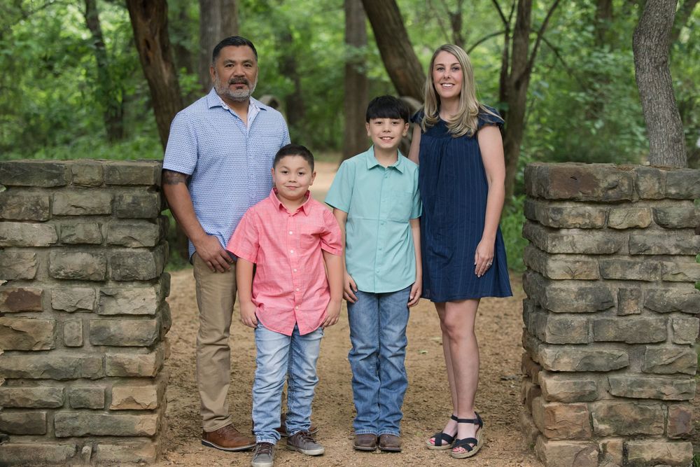 A group stands in front of a stone wall in a wooded area wearing coordinated casual outfits.