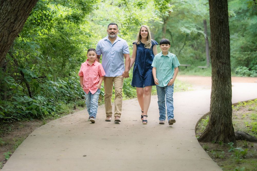 A couple walking with two children on a tree-lined path during summer, all dressed casually.