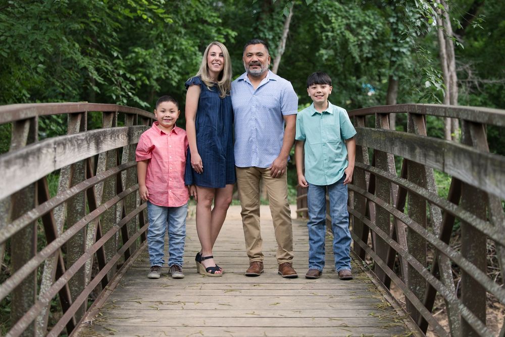 A family of four standing together on a wooden footbridge surrounded by lush green foliage.