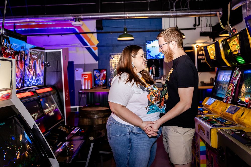Couple shares a romantic moment among retro arcade games with neon lights glowing in the background.