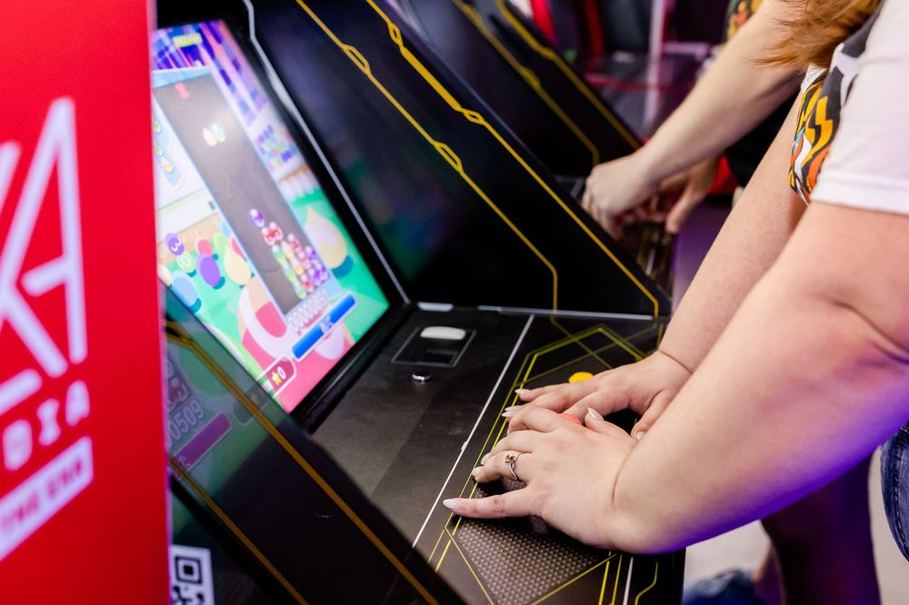 Hands on arcade game controls with neon lighting and bright display screen in a gaming arcade.