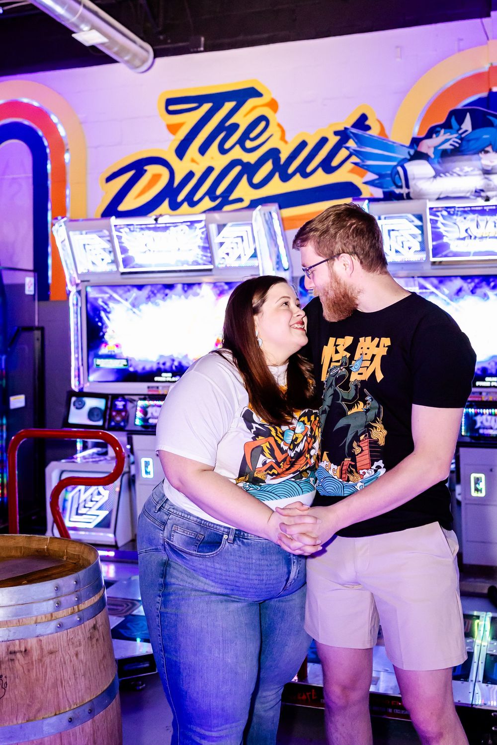 Couple sharing a romantic moment at The Dugout arcade bar with neon signage and gaming machines in the background.