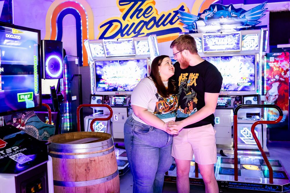 A couple shares a romantic moment in a purple-lit arcade with vintage gaming machines and a neon sign in the background.