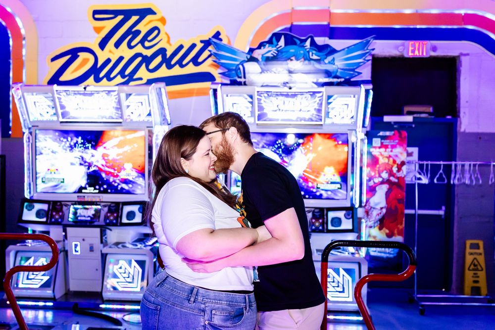 Two people embrace in romantic moment at arcade with neon sign and gaming machines in background.