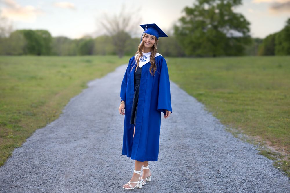 UGA-bound senior smiling during outdoor graduation session in cap and gown on a gravel path in Athens, GA - Senior photographer in Athens