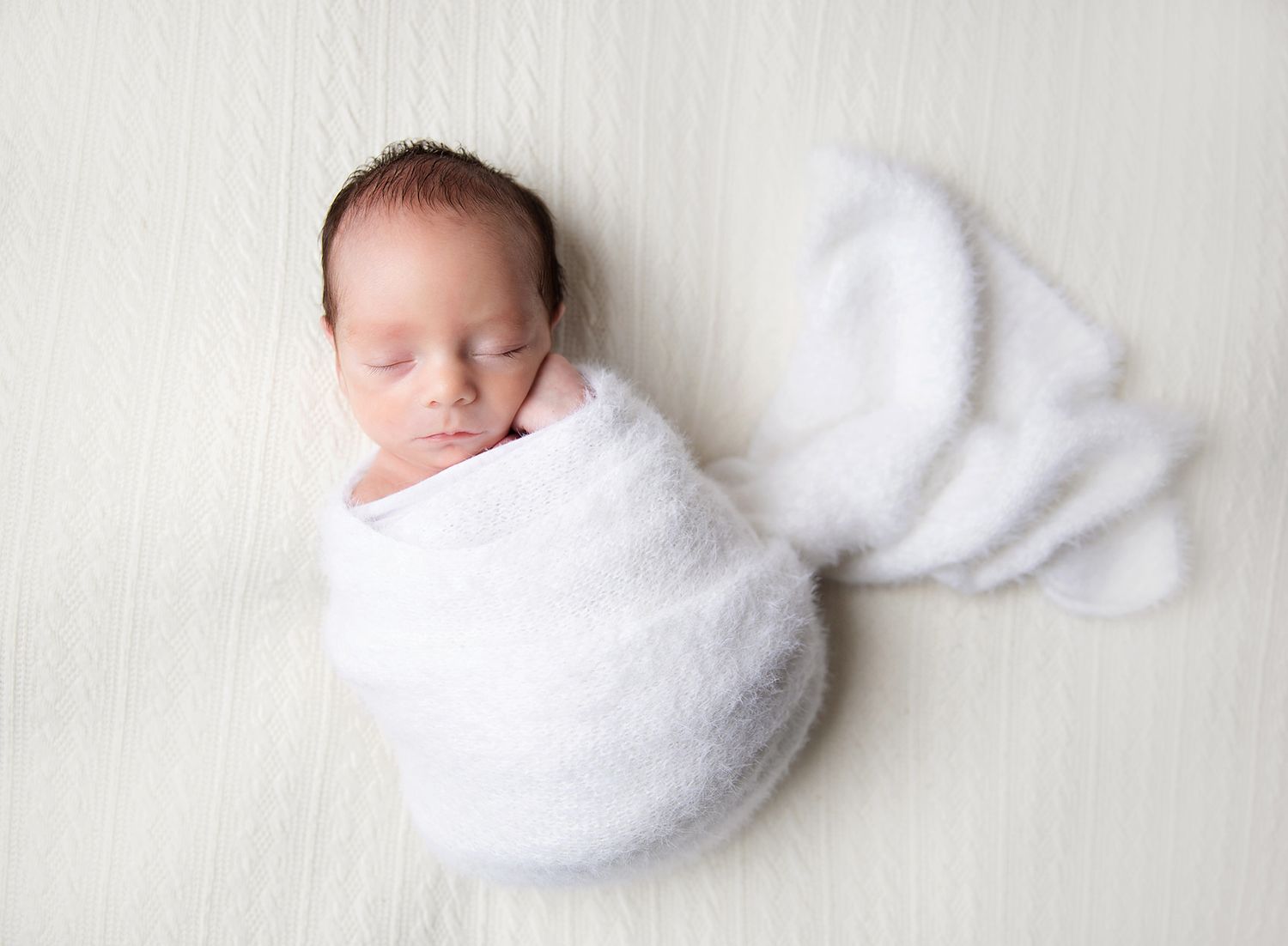 A delicate newborn photo series showing baby swaddled in soft white blanket against pale neutral background. At a Bexley newborn studio