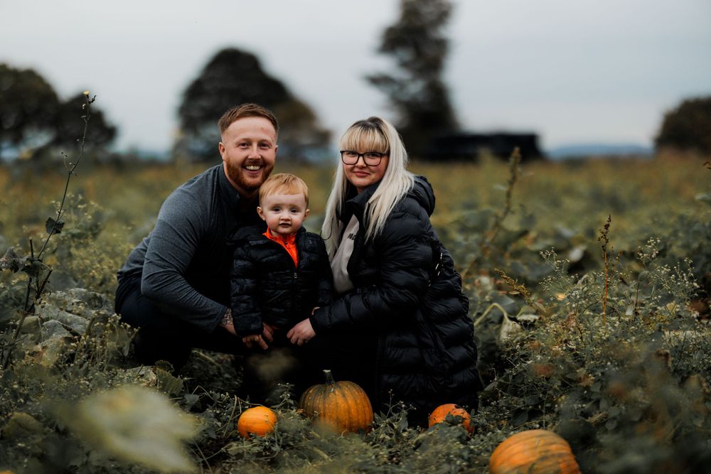 A family poses together among pumpkins in an autumn field.