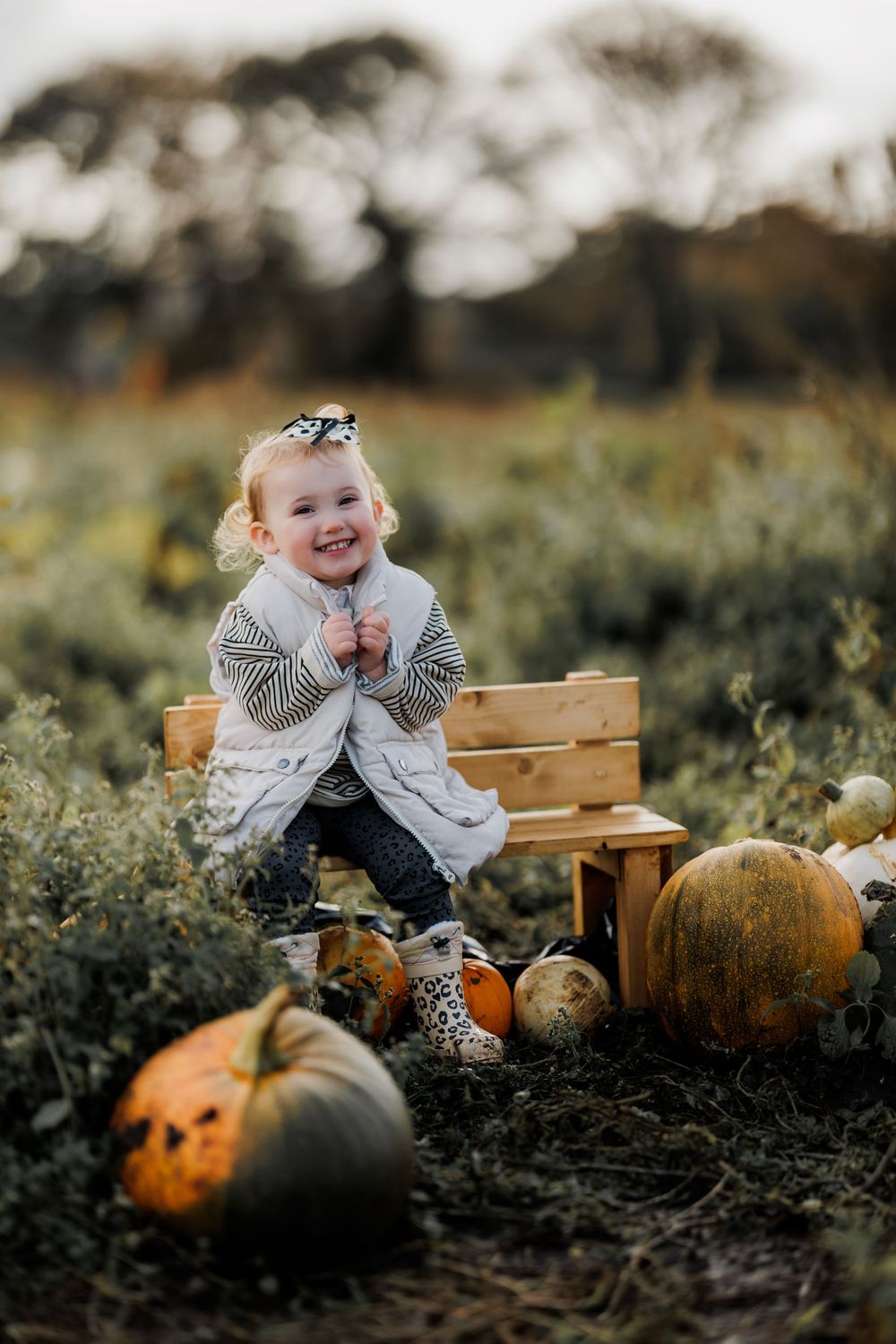A joyful autumn scene with a child sitting on wooden crates surrounded by colorful pumpkins in a field.